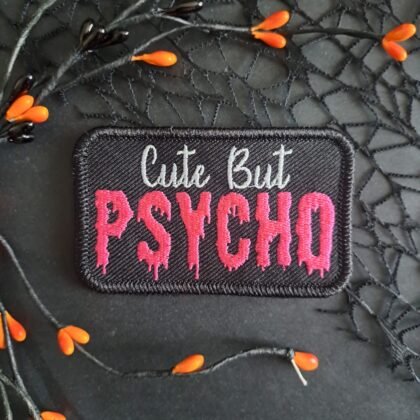 Cute But Psycho patch in pink gothic embroidery on black fabric background