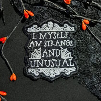 Strange and Unusual gothic iron-on patch styled on black lace fabric with dark aesthetic lighting