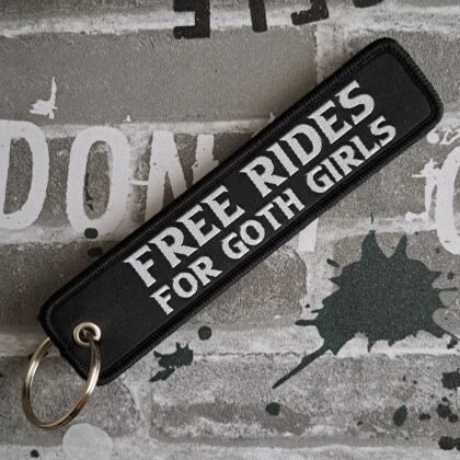Black gothic fabric keytag with white text reading “Free Rides For Goth Girls” attached to metal keyring on dark grunge background