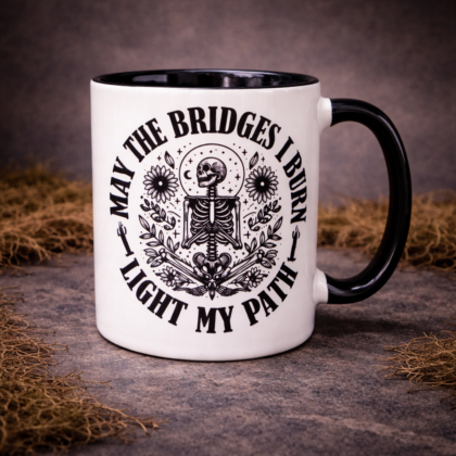 Gothic skeleton mug with May The Bridges I Burn Light My Path design on black handle ceramic coffee cup on dark textured background