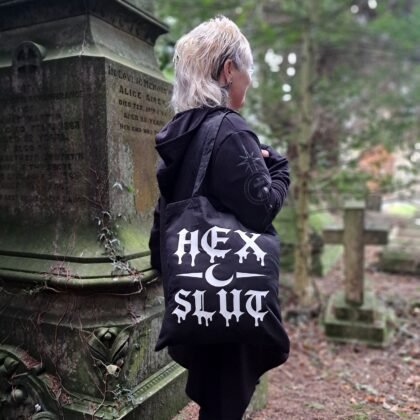 black goth tote bag with bold hex slut gothic lettering worn in atmospheric graveyard setting