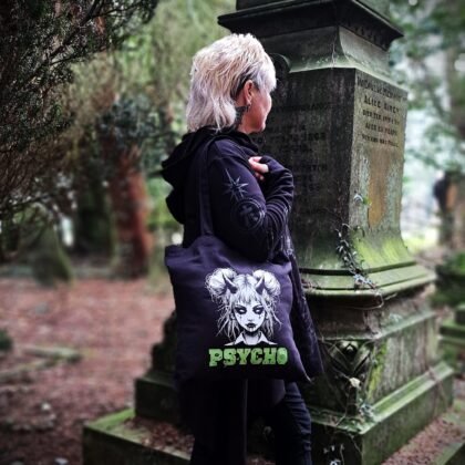 Black gothic tote bag with horned goth girl illustration and psycho lettering worn in woodland graveyard setting