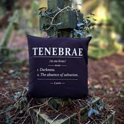 Tenebrae gothic cushion cover with Latin dictionary style darkness definition in white on black Fairtrade cotton displayed on an ivy covered grave cross.