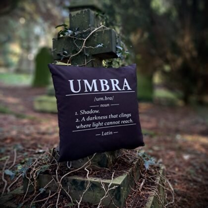 Umbra gothic cushion cover with Latin dictionary style shadow definition printed in white on black Fairtrade cotton displayed on an ivy covered grave cross.