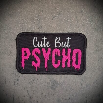 Cute But Psycho patch in pink gothic embroidery on black fabric background