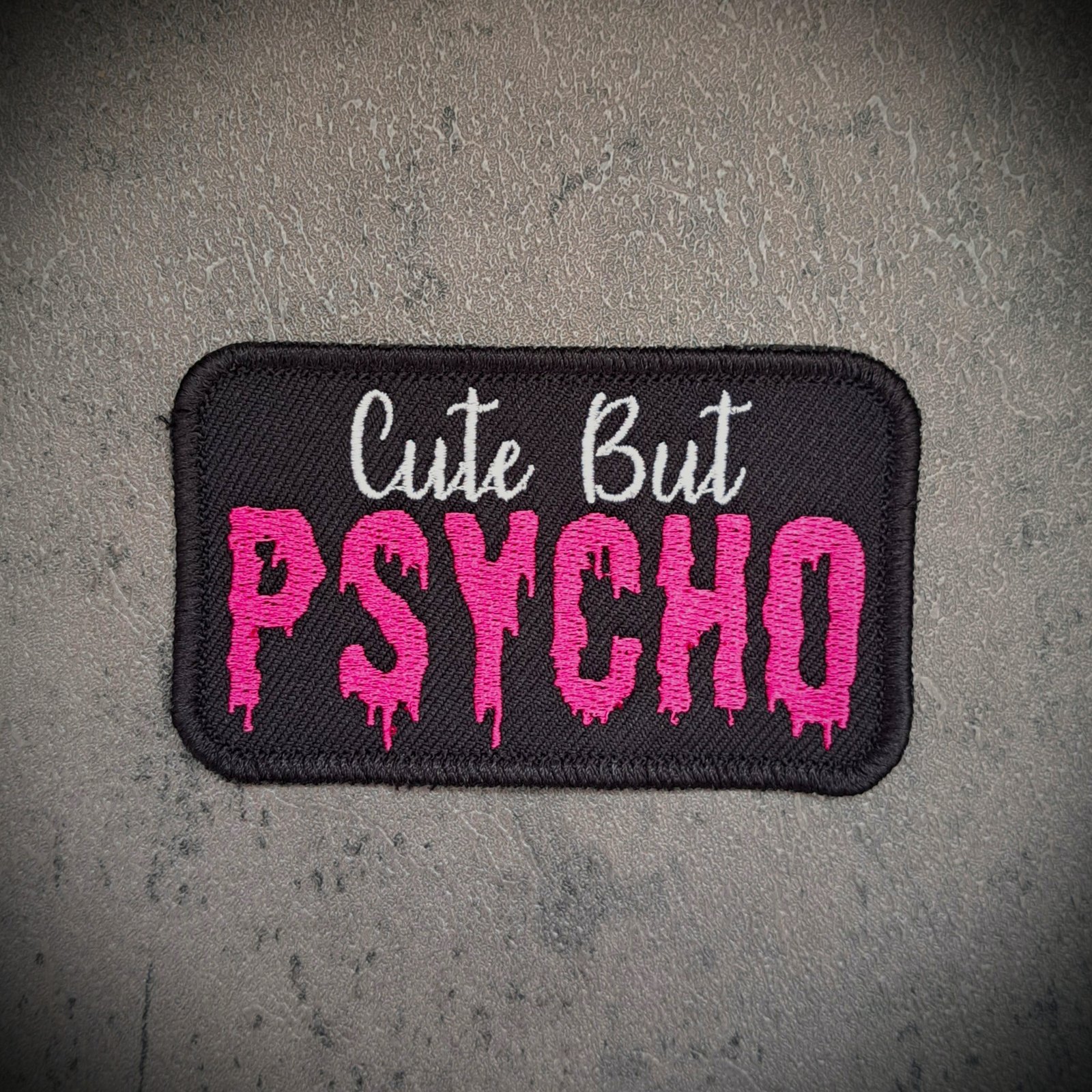 Cute But Psycho patch in pink gothic embroidery on black fabric background