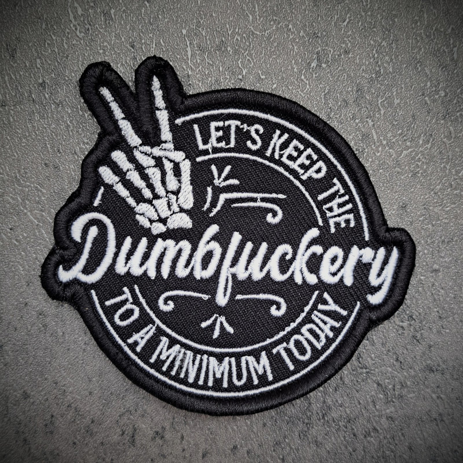 Dumbfuckery embroidered patch with skeleton hand design in black and white
