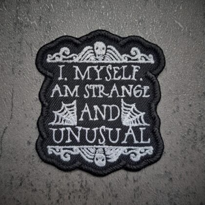 Strange and Unusual gothic iron-on patch styled on black lace fabric with dark aesthetic lighting