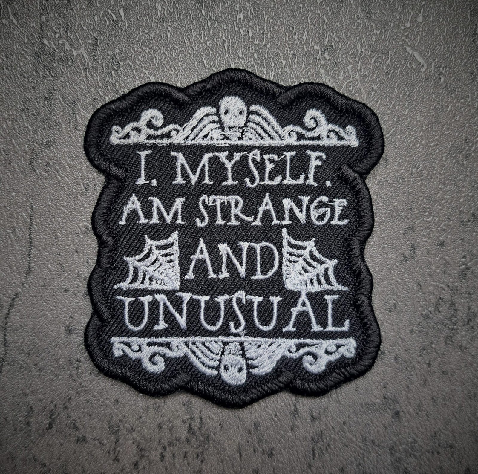 Strange and Unusual gothic iron-on patch styled on black lace fabric with dark aesthetic lighting