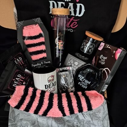 A flat lay view of the open Dead Cute goth gift box contents including skull mug, coffin socks, and black rose candle in black paper shred.