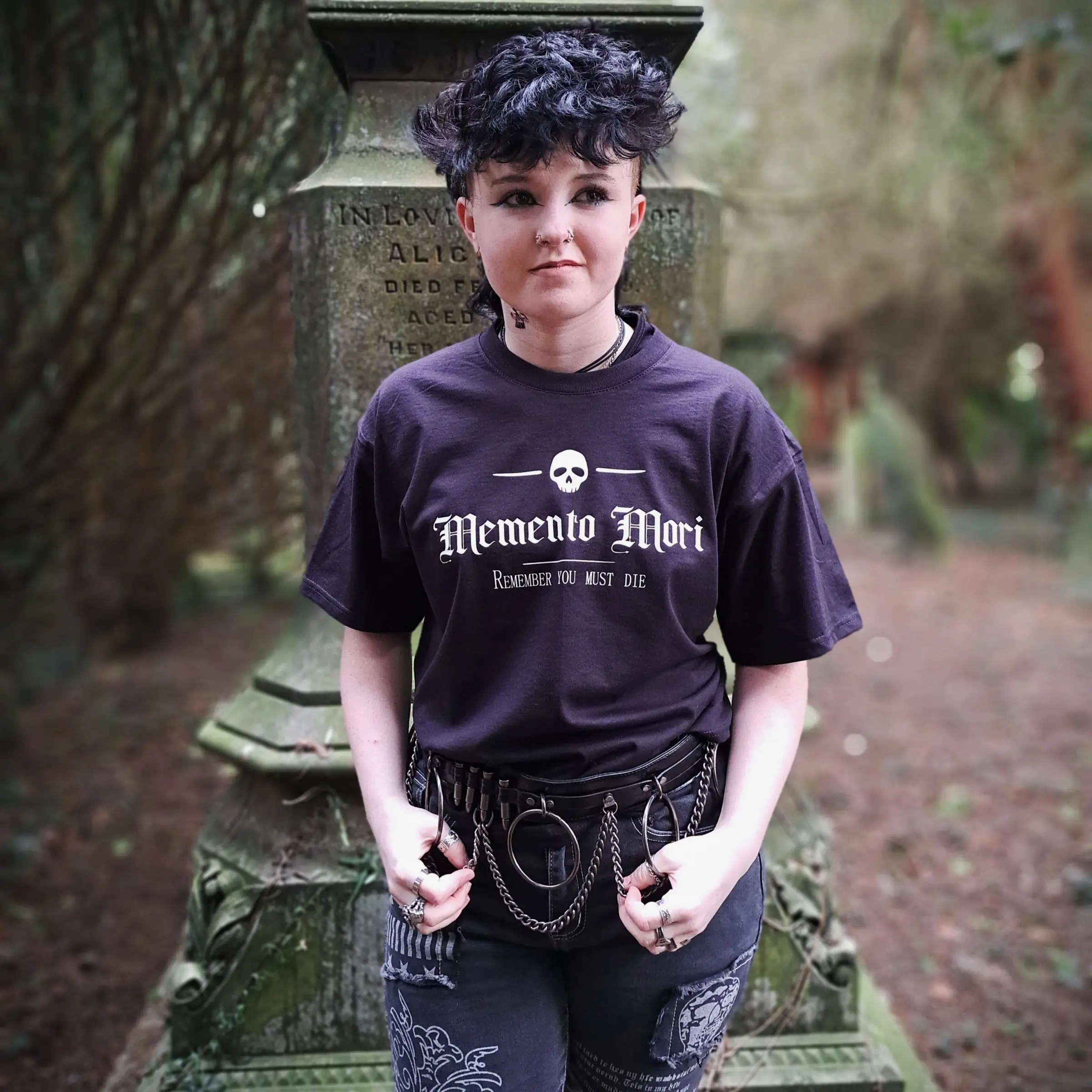 Memento Mori gothic t-shirt in black, featuring a white skull and Remember You Must Die print, modelled beside a gravestone.